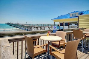 Ein Restaurant am Strand mit Terrassenplätzen mit Blick auf den Ozean und einem Pier im Hintergrund.