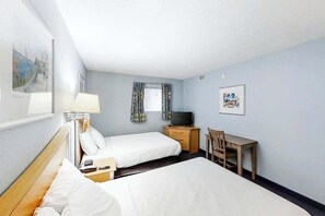 Ein Hotelzimmer mit zwei Betten, einem Schreibtisch, einem Sessel, einem Fernseher und Bildern an den Wänden.