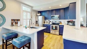 Una cucina moderna con mobili blu scuro, un piano di lavoro bianco e due sgabelli da bar con sedute a fantasia blu.
