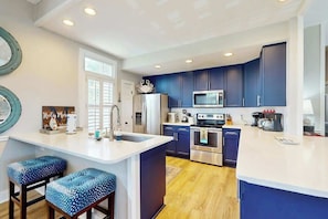 A modern kitchen with dark blue cabinets, a white countertop, and two bar stools with blue patterned seats. - Coastal Escape at Litchfield by the Sea (Litchfield Beach)