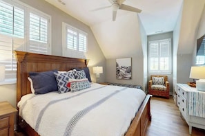 A bedroom with a large bed, a ceiling fan, a chair, a dresser, and a window with blinds. - Coastal Escape at Litchfield by the Sea (Litchfield Beach)