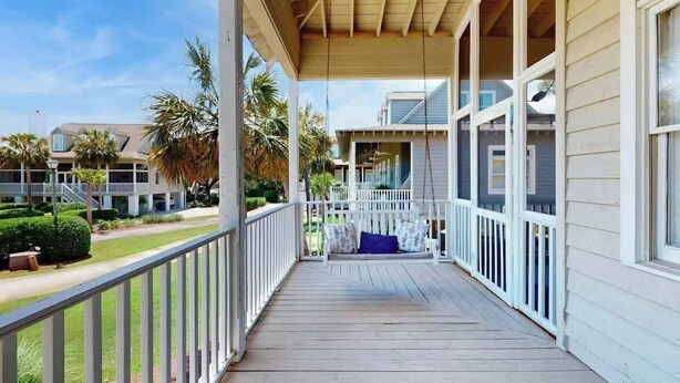 Un portico riparato con una sedia a dondolo, ringhiere bianche e vista su una zona residenziale con case e palme.