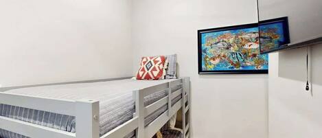 Une chambre avec un lit superposé, un tableau encadré au mur et une prise de courant.