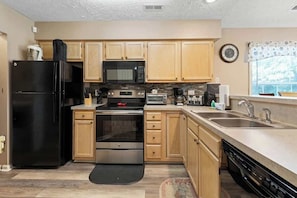 A modern kitchen with wooden cabinets, stainless steel appliances, and a large window. - Coastal Charm Unit 2G (Myrtle Beach)