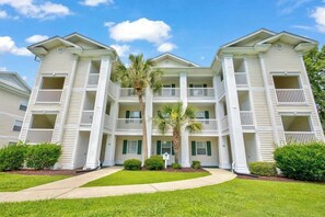 A multi-story hotel with a central courtyard, balconies, and a palm tree. - Coastal Charm Unit 2G (Myrtle Beach)