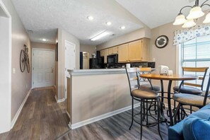A kitchen with wooden cabinets, a central island, and a dining area with chairs. - Coastal Charm Unit 2G (Myrtle Beach)