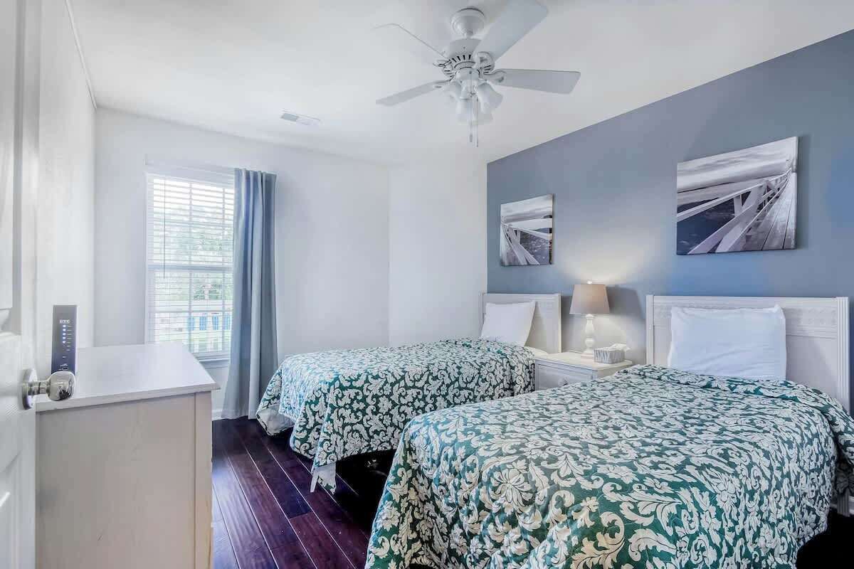 Une chambre d’hôtel avec deux lits, un ventilateur de plafond, une fenêtre avec des rideaux et des œuvres d’art accrochées au mur.