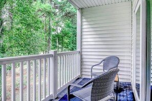 A covered porch with a metal chair and a white railing. - River Oaks Retreat 19C (Myrtle Beach)
