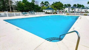 Ein rechteckiger Swimmingpool mit Metallhandlauf an einer Seite, umgeben von einem weißen Zaun und Liegestühlen.