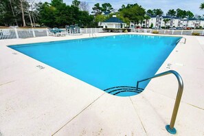 Ein rechteckiger Swimmingpool mit Metallhandlauf an einer Seite, umgeben von einem weißen Zaun und Liegestühlen.