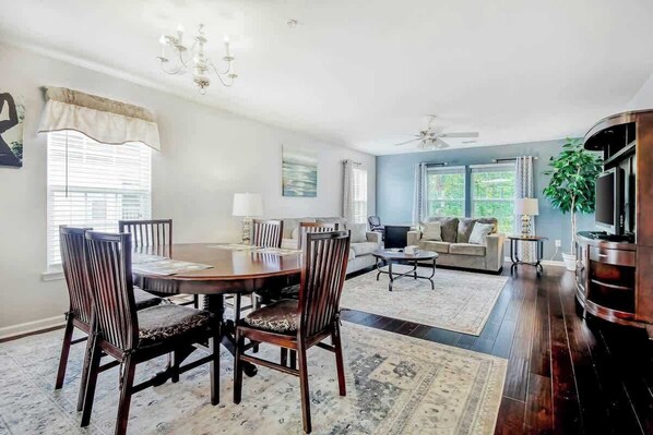A dining area with a round table and chairs, a sofa, a television, and a plant. - River Oaks Retreat 19C (Myrtle Beach)