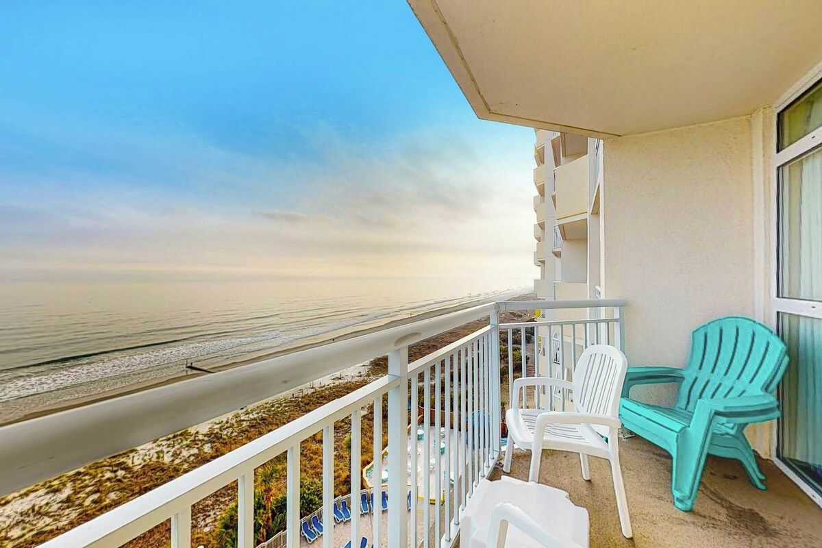 Ein Balkon mit Blick auf den Strand, weiße Stühle und ein türkisfarbener Stuhl.