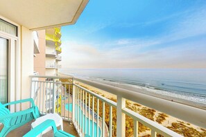 A balcony with a view of the beach, a pool, and a building with yellow balconies. - Bay Watch Resort 0933 (North Myrtle Beach)