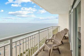 A balcony with a view of the beach and ocean, featuring two Adirondack chairs and a glass door. - Bay Watch Resort 1709 (North Myrtle Beach)