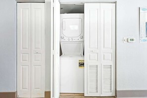 A laundry room with a front-loading washer and dryer, a recycling sign, and a thermostat on the wall. - Bay Watch Resort 1709 (North Myrtle Beach)