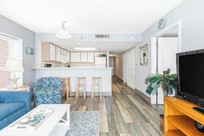 Un saló modern amb un sofà, una taula de centre, un televisor i una zona de cuina amb tamborets.