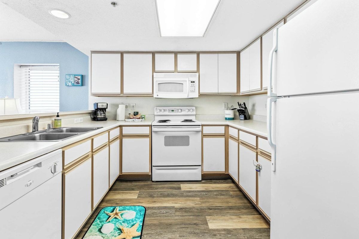 A compact kitchen with white cabinets, a microwave, stove, and a refrigerator.