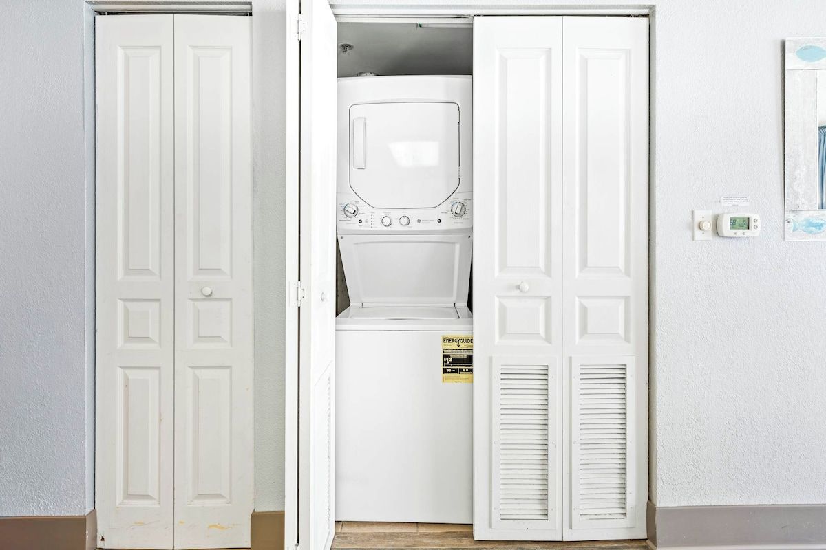 A laundry room with a front-loading washer and dryer, a door with a handle, and a wall-mounted thermostat.