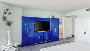 Quarto com cama, televisão, guarda-roupa e uma pequena mesa com aquecedor.