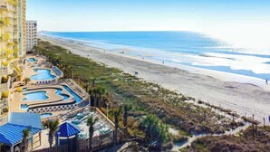 Ein Strandhotel mit mehreren Schwimmbecken, einem Strand und Blick aufs Meer.
