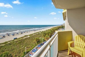 A balcony with a view of a beach, a yellow chair, and a railing. - Bay Watch Resort 0504 (North Myrtle Beach)