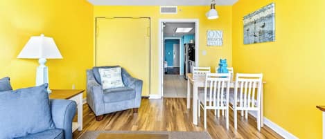 A room with yellow walls, a blue sofa, a wooden coffee table, a dining table with chairs, and a lamp.