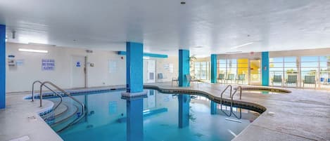 An indoor swimming pool with clear signage, a tiled floor, and a view of the outside through large windows.
