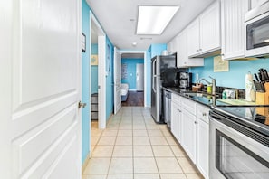 A kitchen with white cabinets, a black refrigerator, and a tiled floor. - Bay Watch Resort 0504 (North Myrtle Beach)