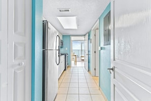 A hallway with a kitchen area, a microwave, and a view of the outside. - Bay Watch Resort 0504 (North Myrtle Beach)