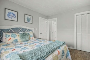 A bedroom with a bed, two framed wall art pieces, a door, and a closet. - Shipwatch Pointe I - J329 (Myrtle Beach)