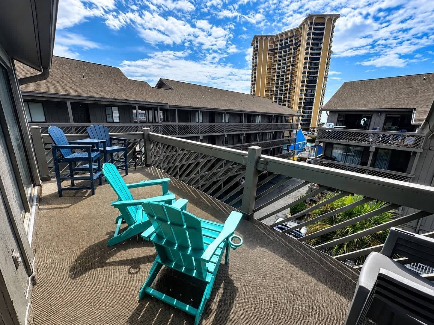 A balcony with Adirondack chairs, a railing, and a view of a high-rise building.