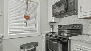 Una cocina con armarios blancos, un horno de acero inoxidable y un microondas encima.