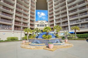Un hotel de varios pisos con un patio central que presenta una fuente de agua, rodeado de balcones.