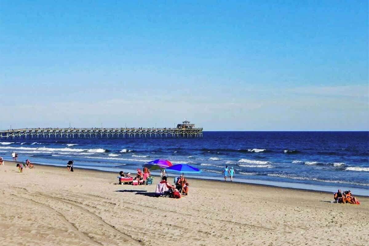 A beach with people, a pier, and umbrellas.