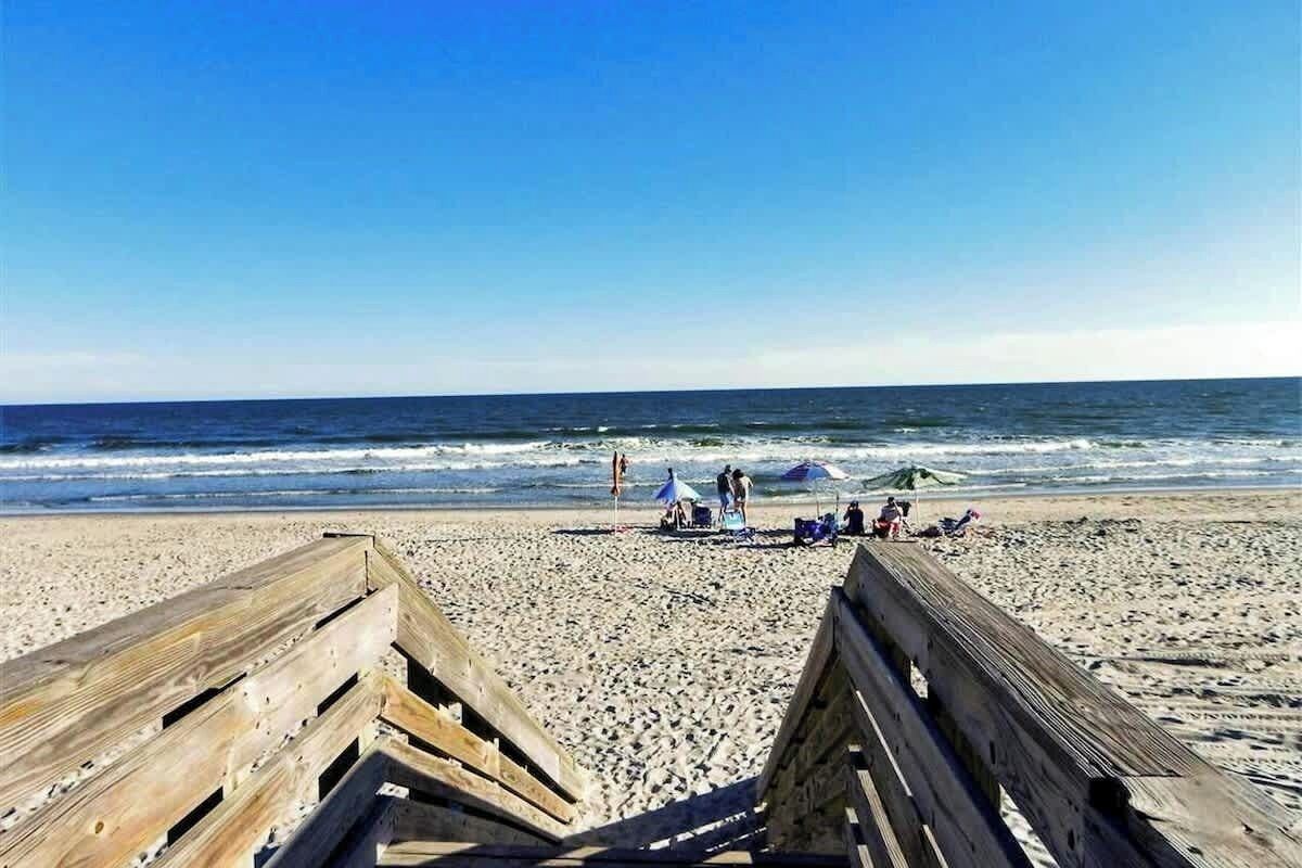 A beach with wooden boardwalks, people relaxing, and umbrellas.