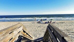 Ein Strand mit Holzbodenbelag, entspannende Menschen und Sonnenschirmen.