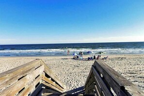 Ein Strand mit Holzbodenbelag, entspannende Menschen und Sonnenschirmen.