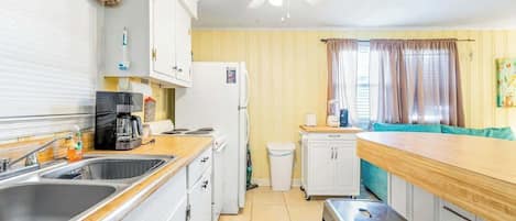 A compact kitchen with a sink, stove, and refrigerator. There is a ceiling fan and a window with curtains.
