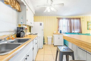 Eine kleine Küche mit Spüle, Herd und Kühlschrank. Ein Deckenventilator und ein Fenster mit Vorhängen sind vorhanden.