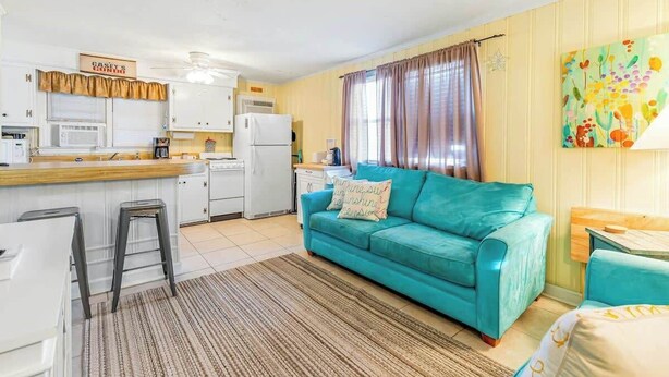 Ein kompakter Wohnbereich mit Küchenzeile, einem blaugrünen Sofa und einem Streifenmuster-Teppich.