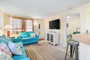 Ein Wohnzimmer mit einem blauen Sofa, einem Fernseher und einer kleinen Essecke.