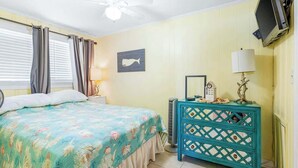Ein Schlafzimmer mit einem Bett, einem Schminktisch, einem Fernseher und einem Deckenventilator.