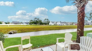 A patio with white chairs, a small table, and a view of a water body and houses in the background. - Eagle Haven H1 Condo (Myrtle Beach)