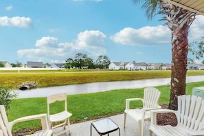 A patio with white chairs, a small table, and a view of a water body and houses in the background. - Eagle Haven H1 Condo (Myrtle Beach)