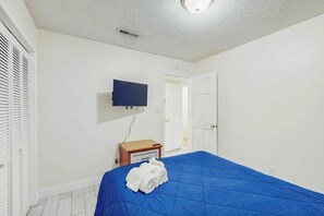 A bedroom with a blue bedspread, a television mounted on the wall, and a door leading to another room. - Eagle Haven H1 Condo (Myrtle Beach)