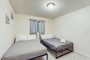 Ein Zimmer mit zwei Einzelbetten, einem fenster mit Vorhängen und einer Deckenleuchte.