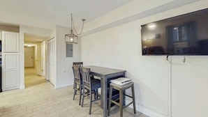 A dining area with a table and chairs, a hanging light fixture, and a television mounted on the wall. - Eagle Haven H1 Condo (Myrtle Beach)
