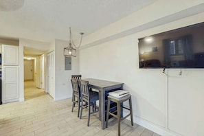 A dining area with a table and chairs, a hanging light fixture, and a television mounted on the wall. - Eagle Haven H1 Condo (Myrtle Beach)