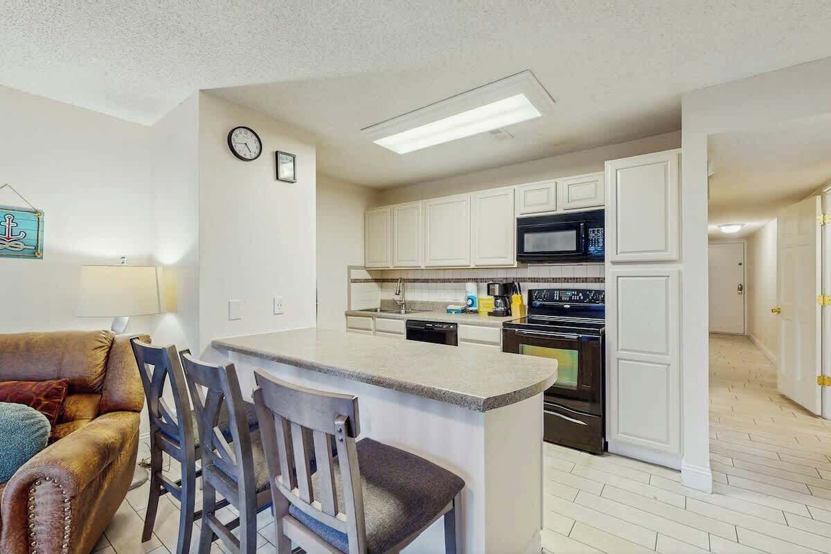 A compact kitchen with white cabinetry, a microwave, an oven, and a small island with bar stools.
