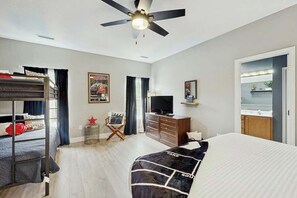 Quarto de hotel com beliche, uma escrivaninha com cadeira, televisão e armário.